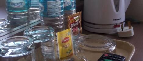 Una bandeja con un control remoto, una bolsita de té Lipton, una cuchara y varias botellas de agua sobre una mesa.
