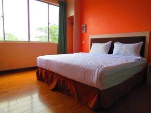 A neatly made bed in a room with wooden flooring and orange walls.
