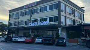 Ein Gebäude mit einem 'Care Care'-Schild, mehreren Etagen und parkenden Autos vor der Fassade.