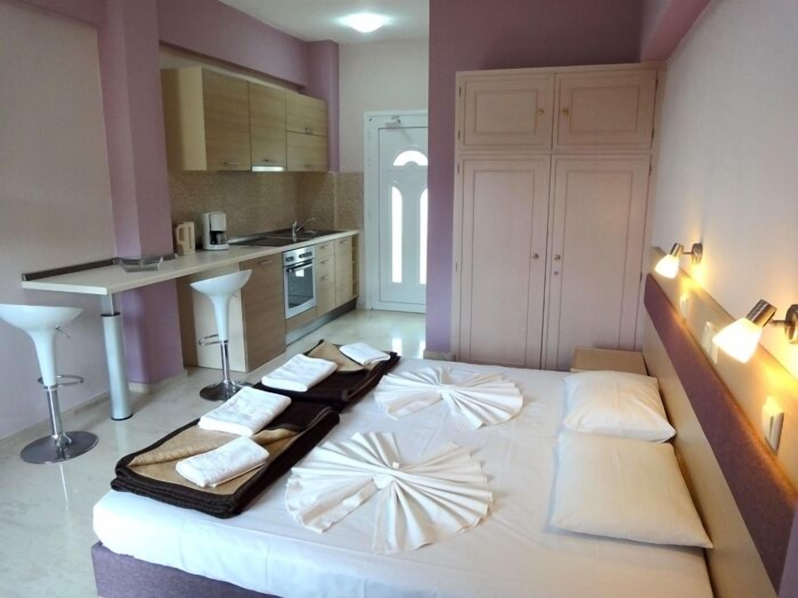 A hotel room with a bed, a small kitchenette, a bathroom, and a view of the outside.