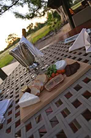 A table with a wooden cutting board, various cheeses, bread, and a bottle of wine.