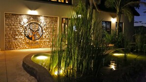 A building with a stone facade, a logo with a horse and rider, and a water feature with tall grasses. - La Rochelle (Tsumeb)