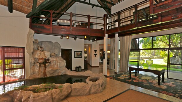 A spacious lobby with a large window, a stone water feature, and a wooden bench. - La Rochelle (Tsumeb)