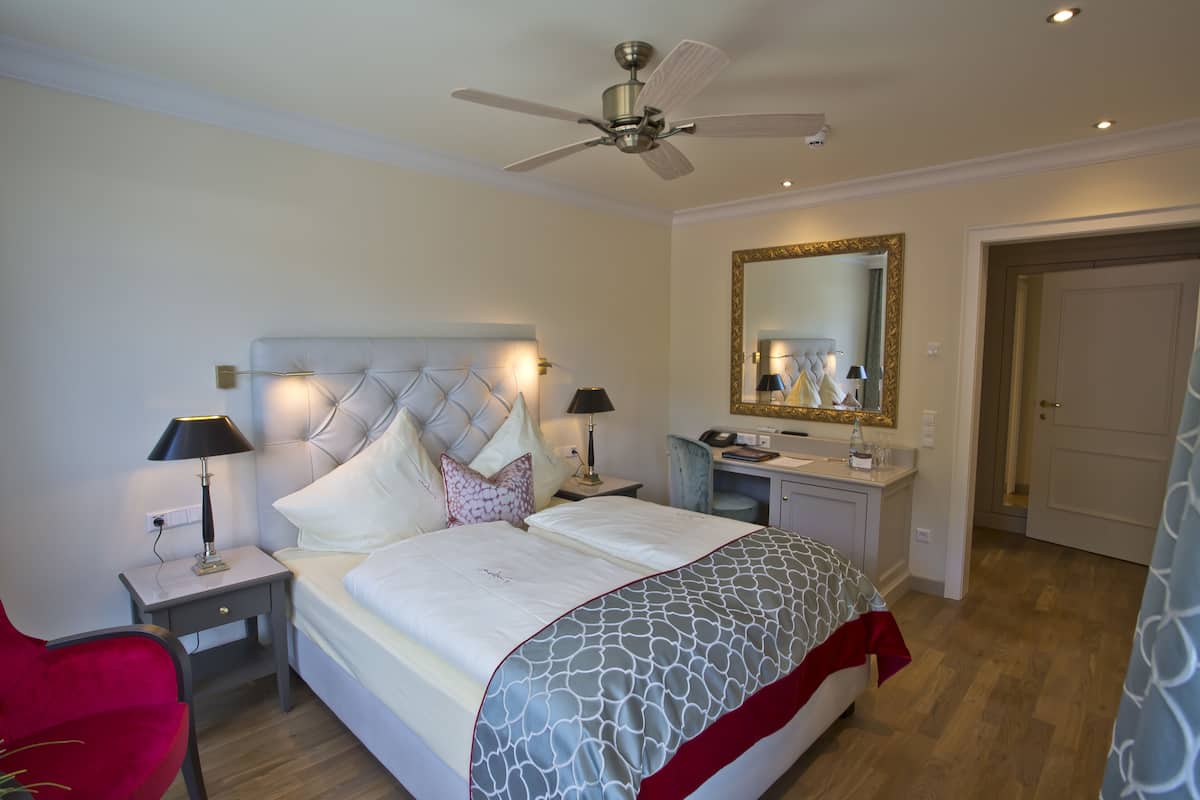 Een slaapkamer met een bed, nachtkastjes, een bureau, een spiegel en een deur.