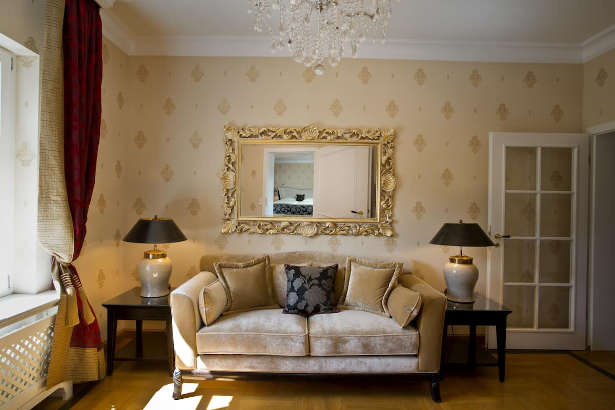 Een kamer met een beige bank, twee lampen, een spiegel en een kroonluchter.