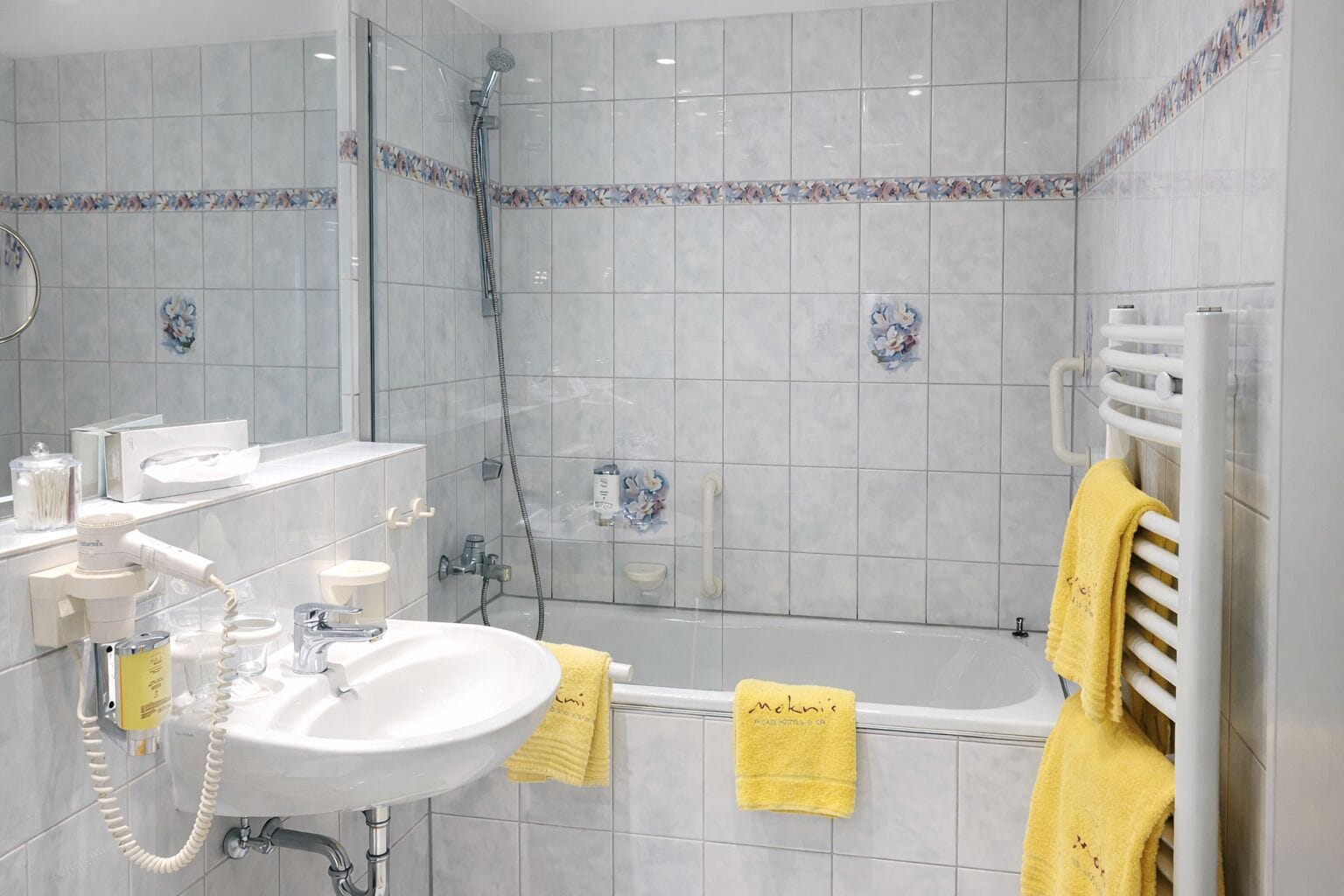 Un baño moderno con ducha de vidrio, lavamanos blanco y toallero con toallas amarillas.