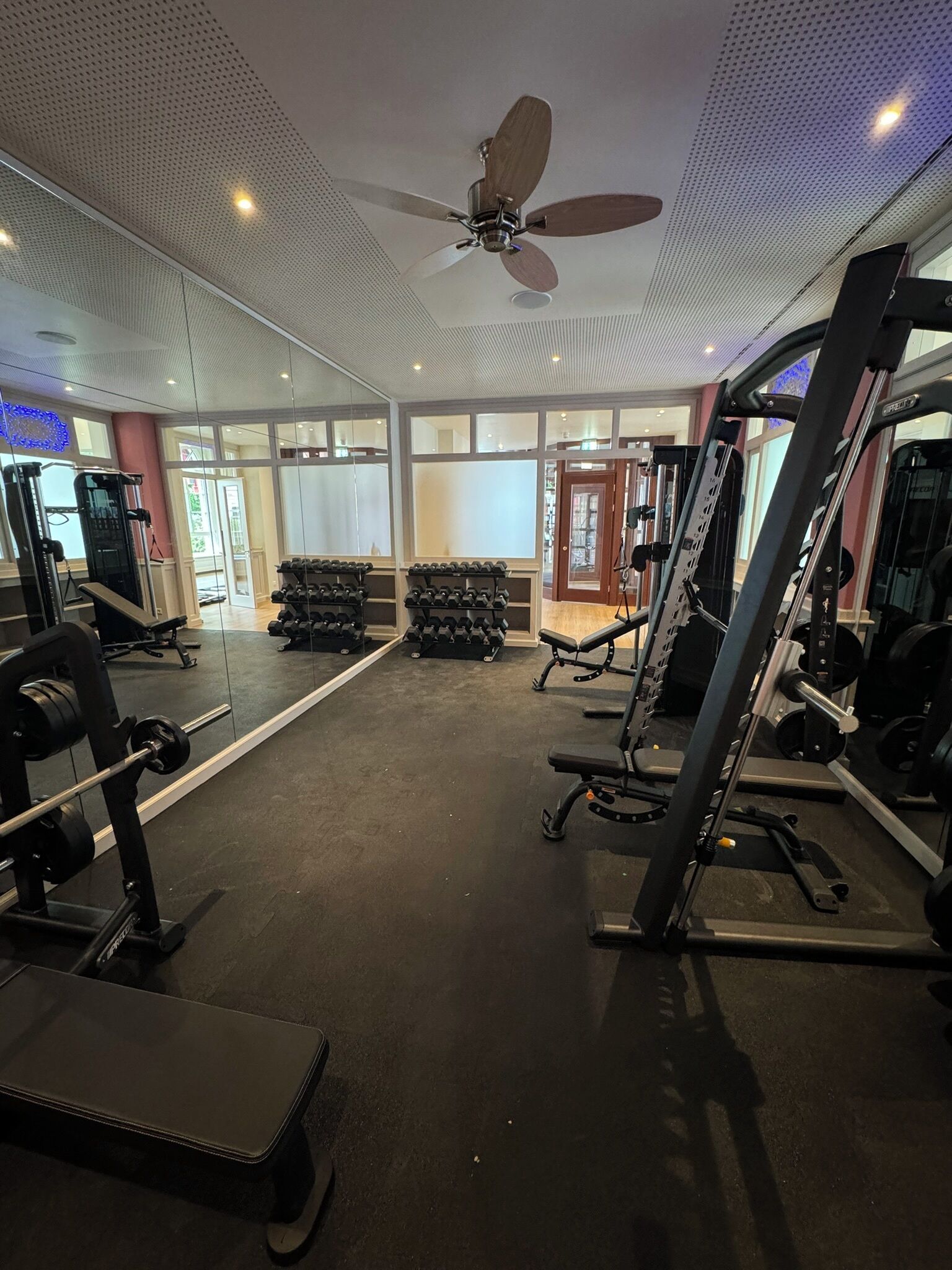 A gym with various exercise equipment, a ceiling fan, and a large mirror.