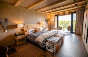 Un dormitorio espacioso con una cama grande, cabecera de madera, mesita de noche y vistas al exterior a través de un ventanal.