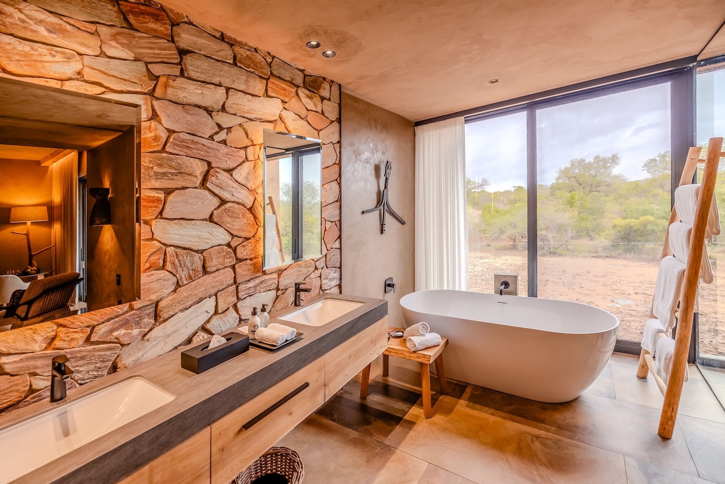 A modern bathroom with stone walls, a large bathtub, and a view of the desert.