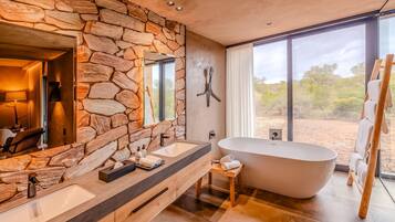 A modern bathroom with stone walls, a large bathtub, and a view of the desert.