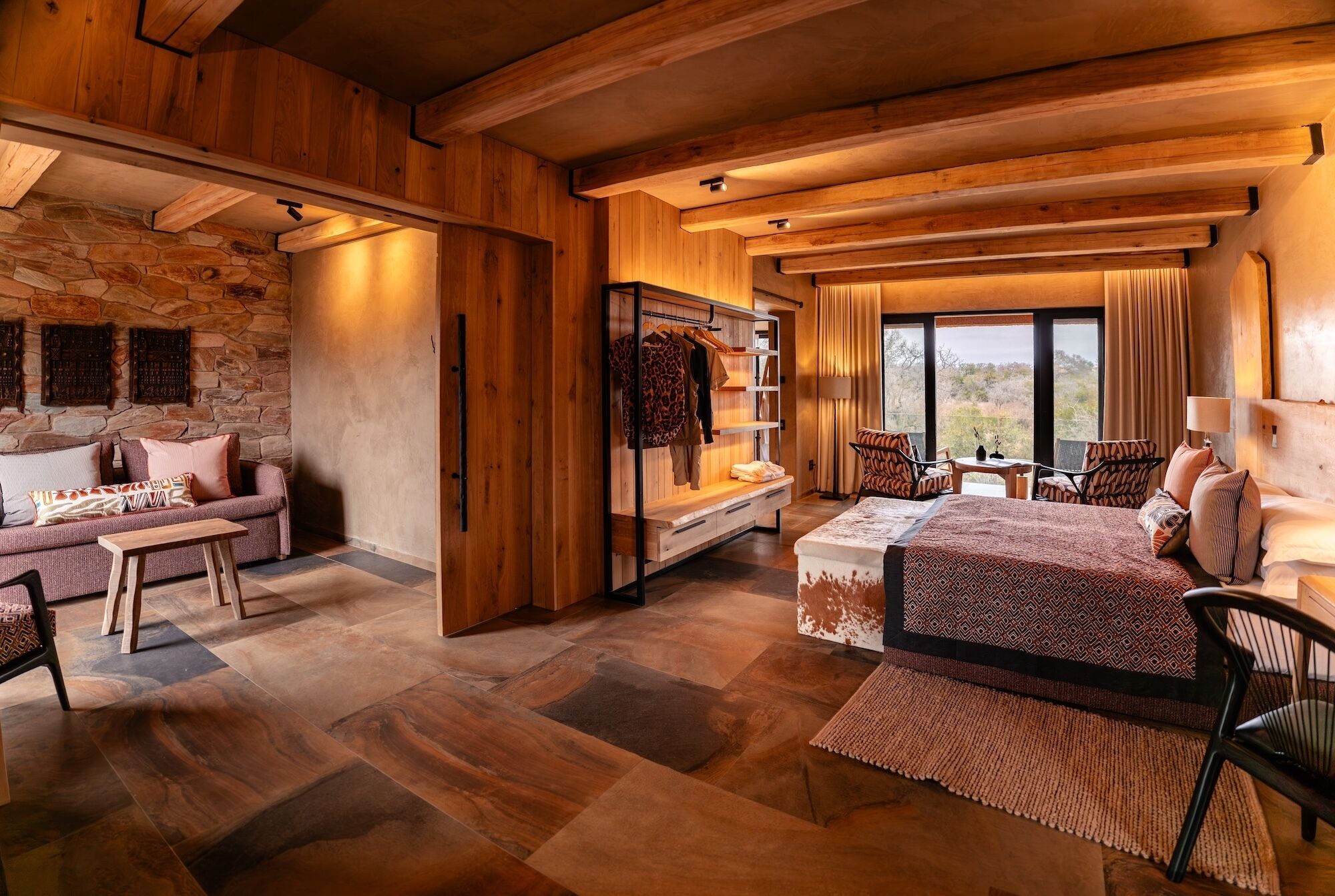 A spacious room with a stone wall, wooden ceiling, and a large bed with patterned bedding.
