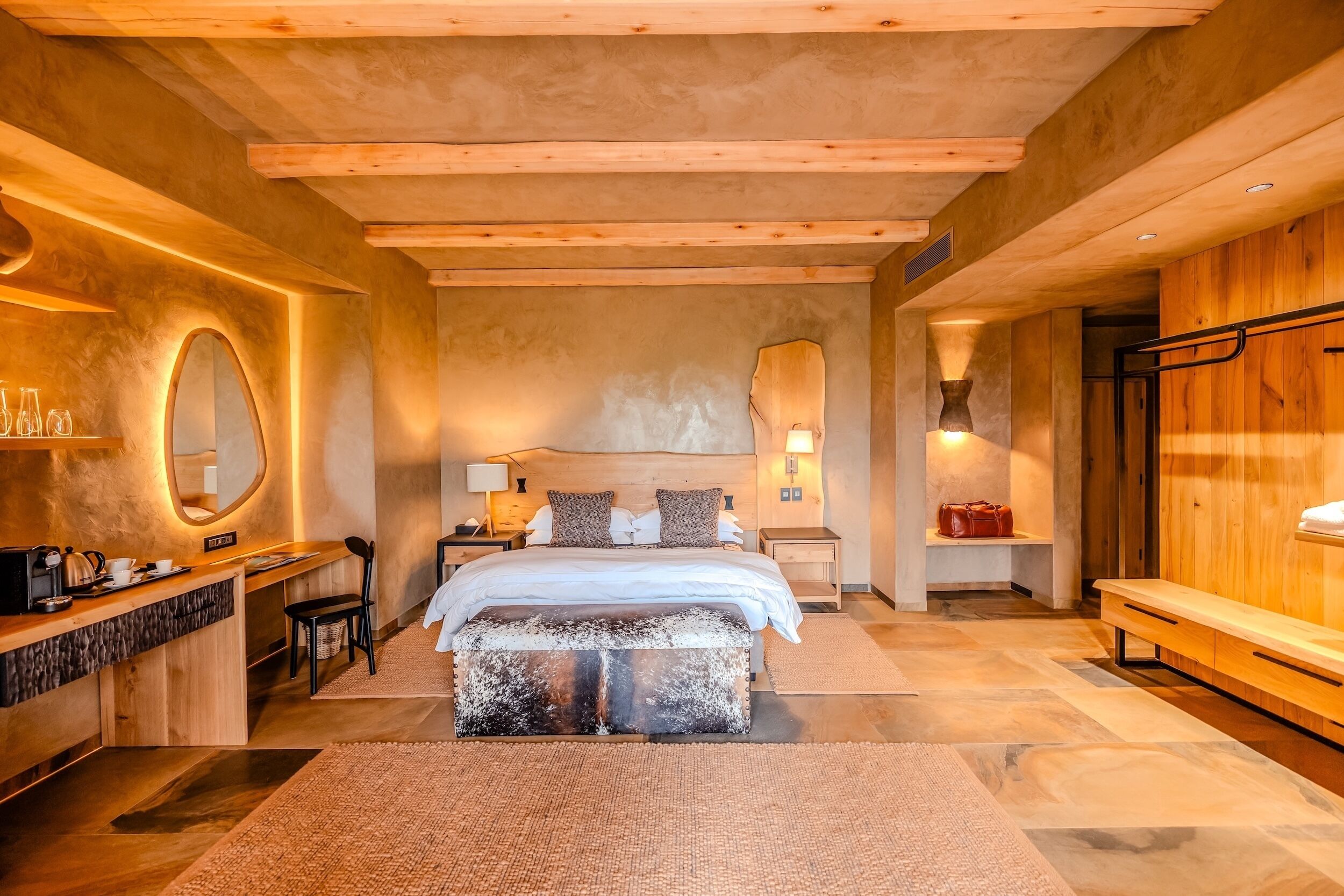 A modern bedroom with a large bed, wooden headboard, bedside tables, a desk, and a bench.