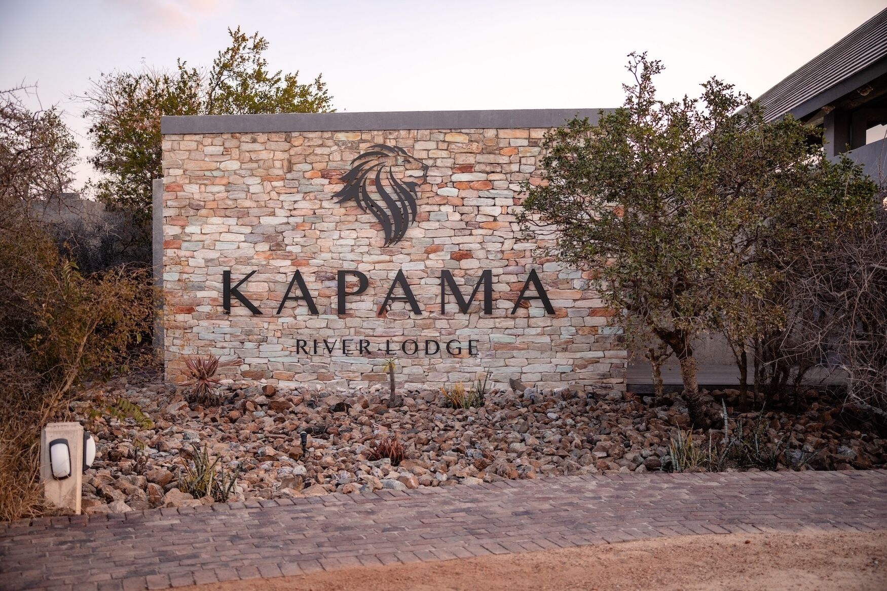 Un mur de pierre sur lequel est inscrit le texte « KAPAMA RIVER LODGE » et au-dessus duquel figure un logo.