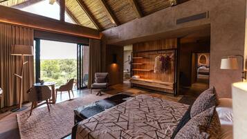 A modern bedroom with a large bed, a seating area with a chair and a table, a wardrobe, and a view of the outdoors.