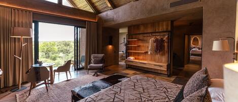 Une chambre moderne avec un grand lit, un coin salon comprenant une chaise et une table, une armoire et une vue sur l’extérieur.