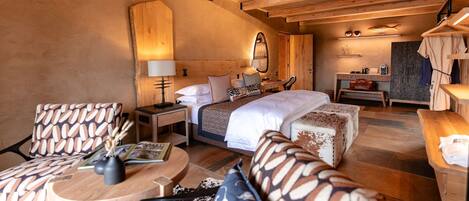 Ein gemütliches Schlafzimmer mit einem großen Bett, einem Holz-Kopfteil, einem Nachttisch mit Lampe, einem kleinen Schreibtisch und einem Sessel mit gemusterten Kissen.