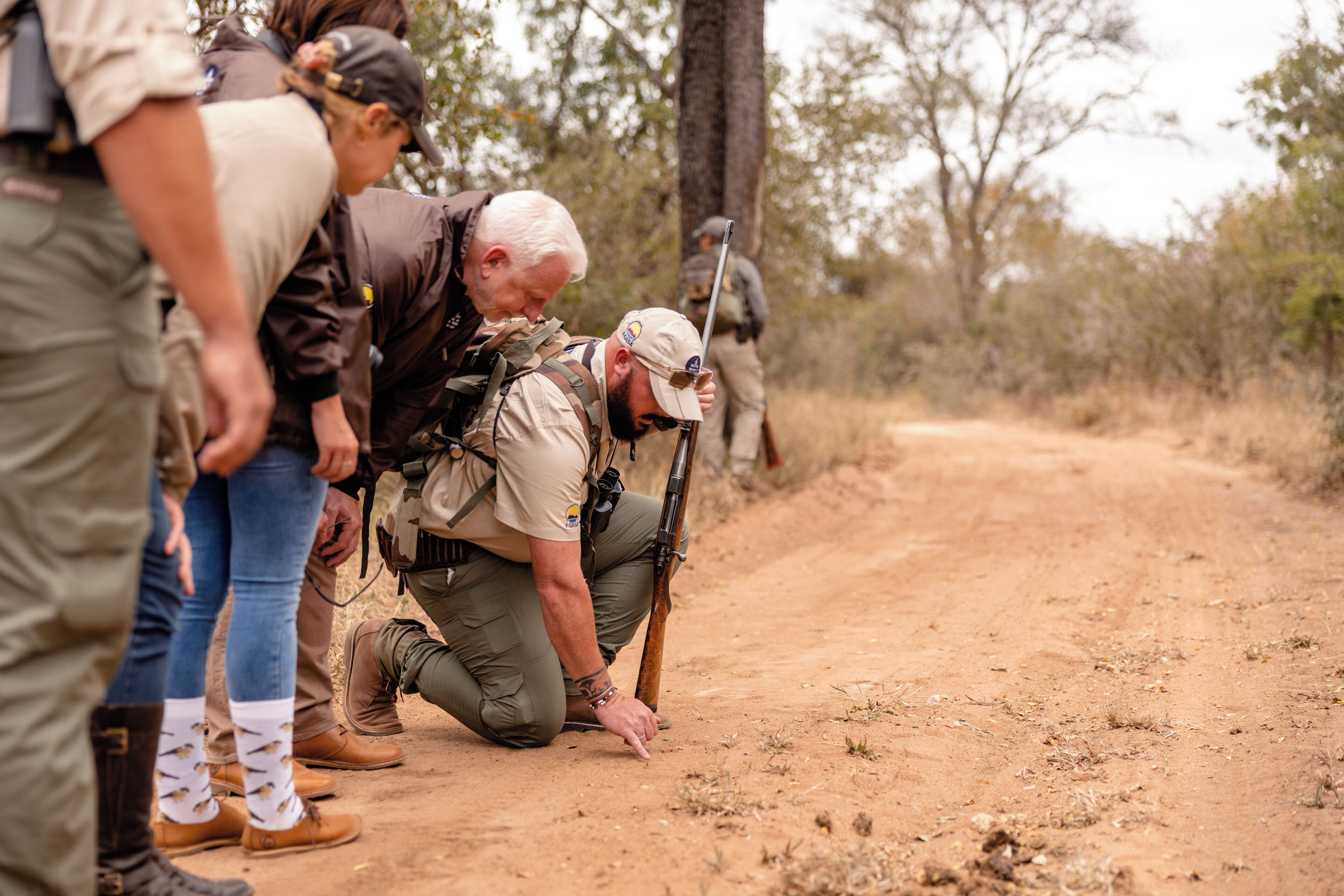 Un grupo de personas vestidas para actividades al aire libre en un sendero de tierra, con árboles al fondo.