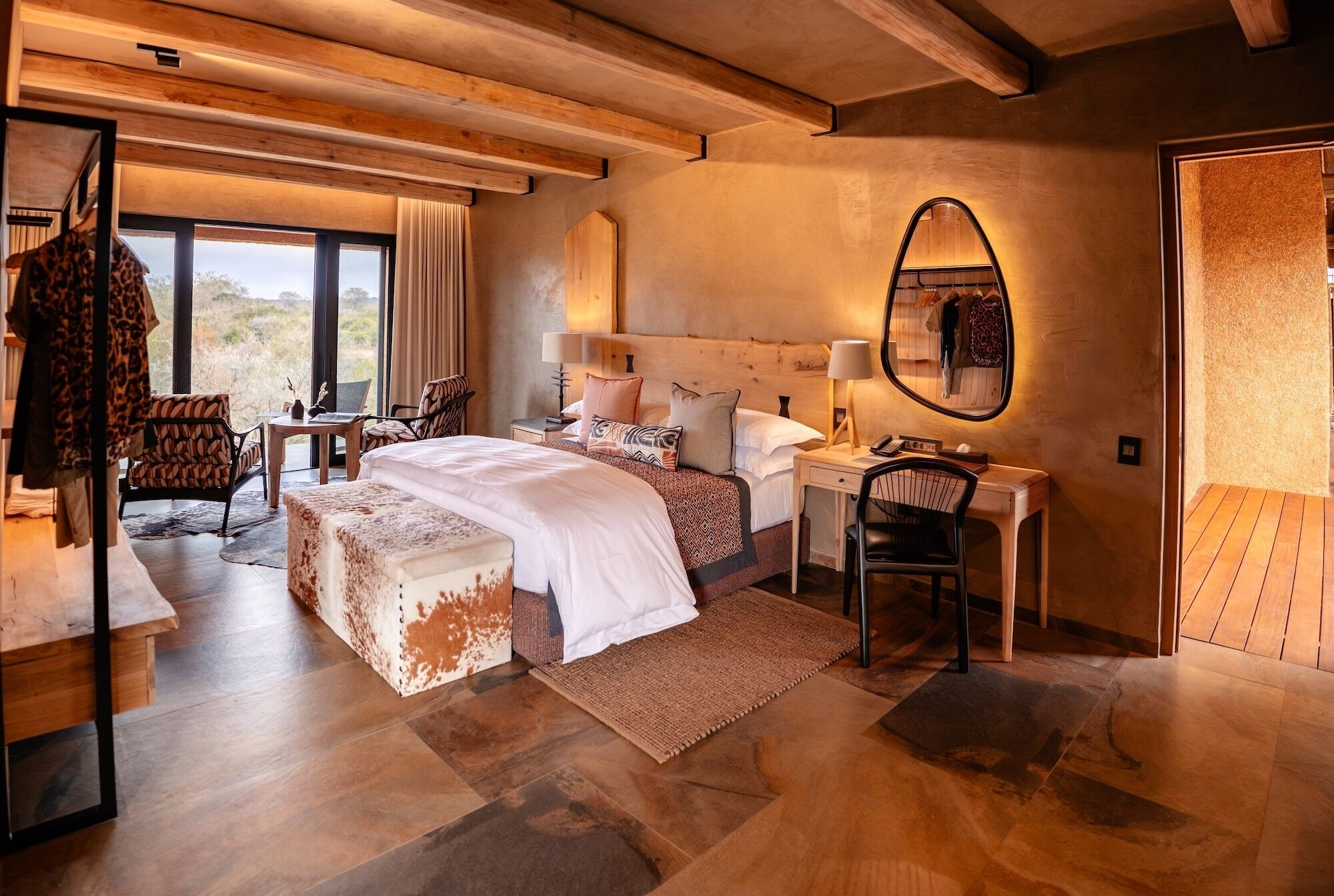 A modern bedroom with a large bed, a desk, and a chair. There is a window with curtains and a view of the outdoors.
