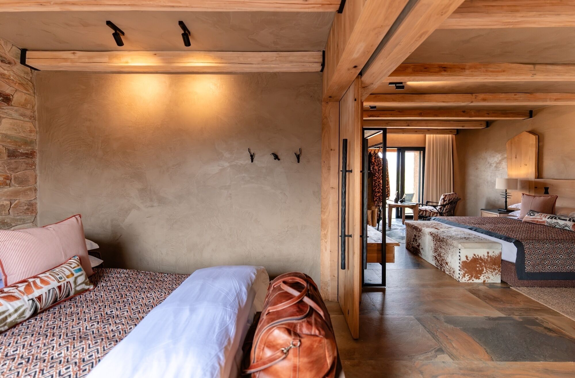 Una habitación de hotel con pared de piedra, una cama con ropa de cama estampada, un bolso de cuero y techo de madera.