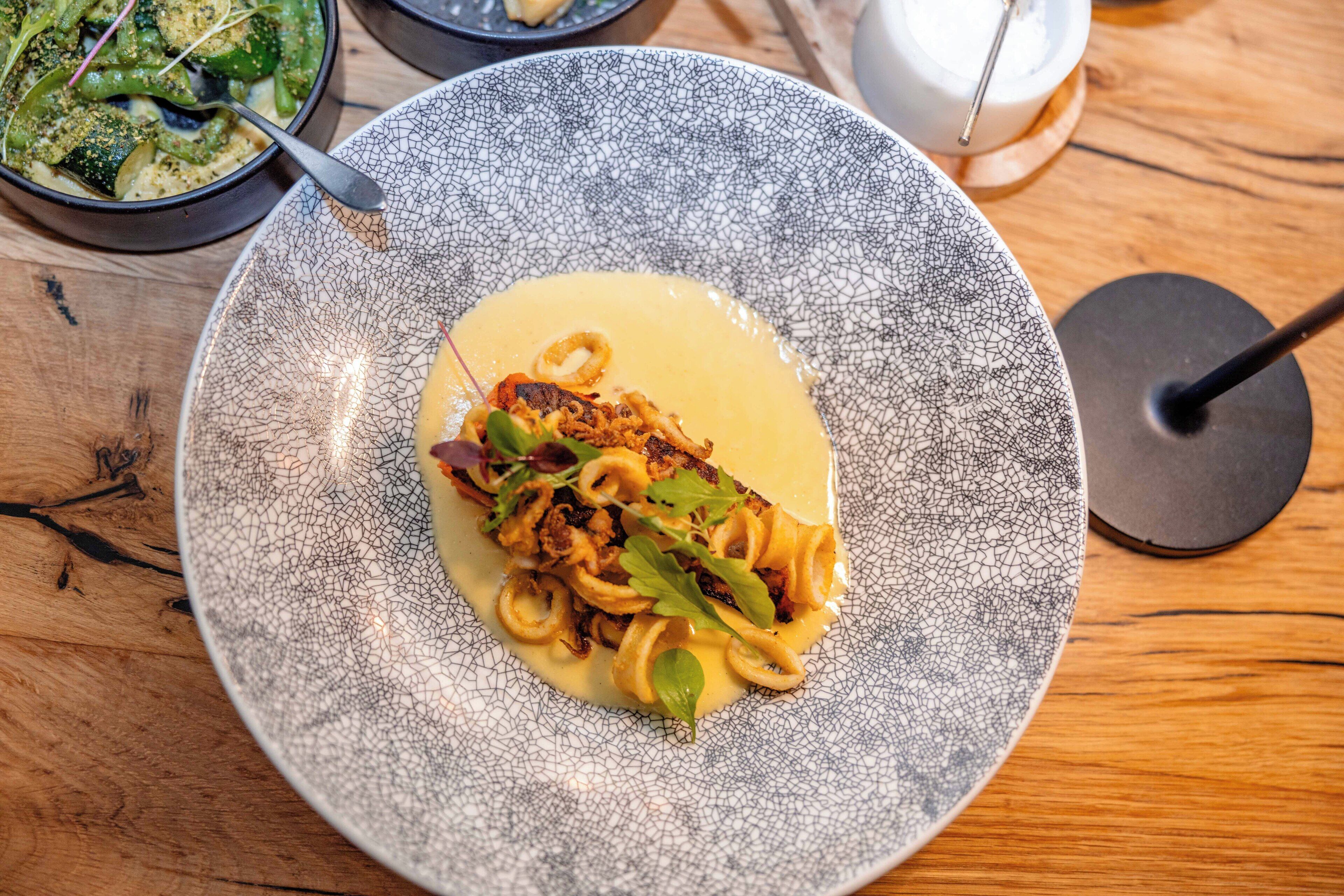A plate of pasta with a creamy sauce and garnishes, served on a textured ceramic plate.