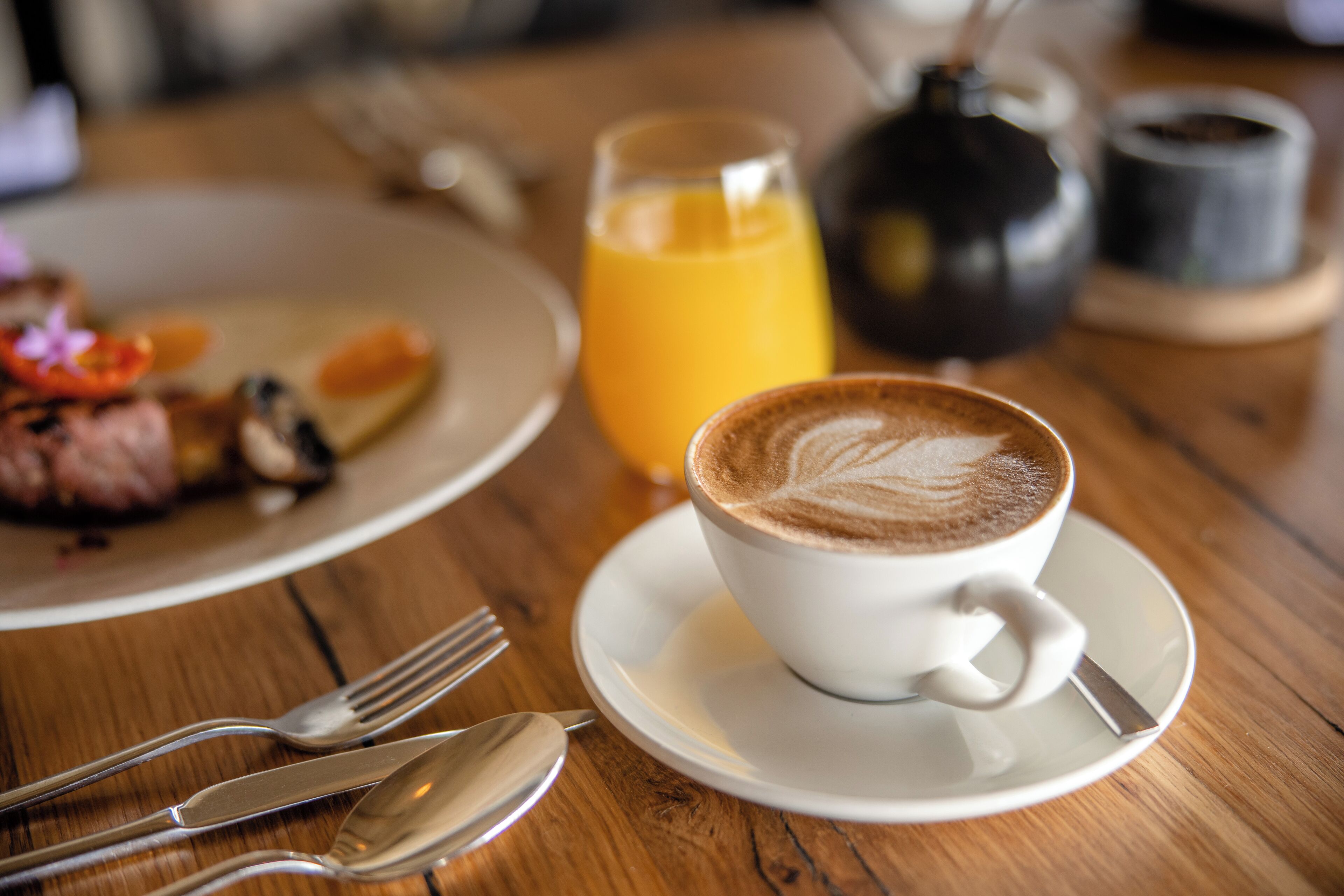 A wooden table with a white cup of coffee, a glass of orange juice, and a plate of food.