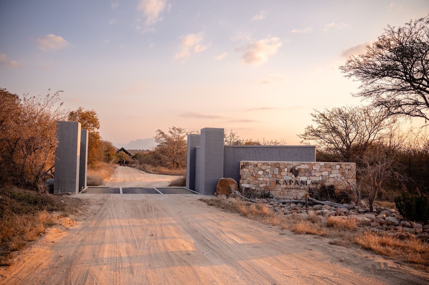 A dirt road leading to a gated entrance with a stone sign reading 'KAPAMA River Lodge.'