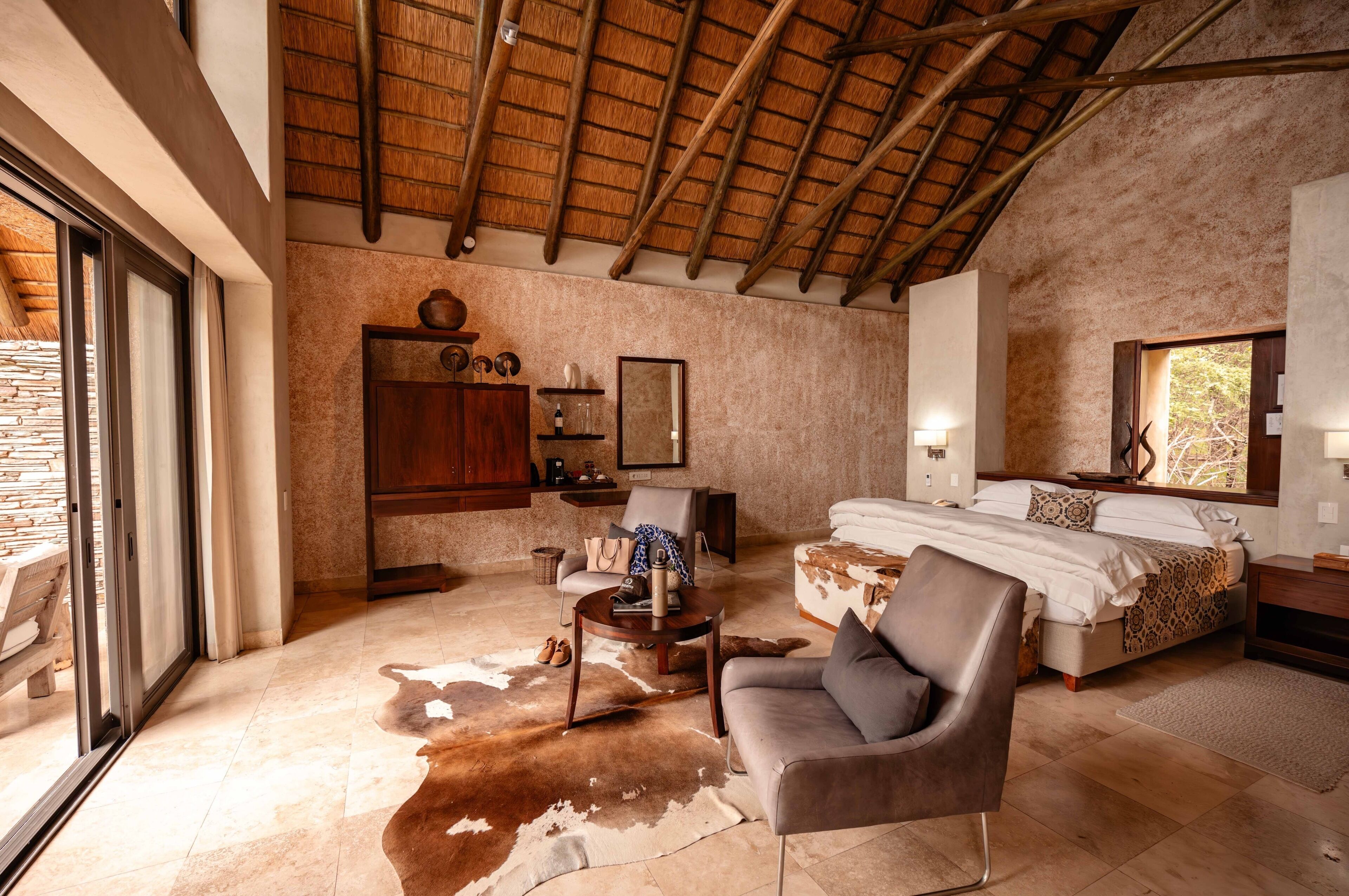 A spacious bedroom with a large bed, a wooden wardrobe, a leather armchair, and a cowhide rug.