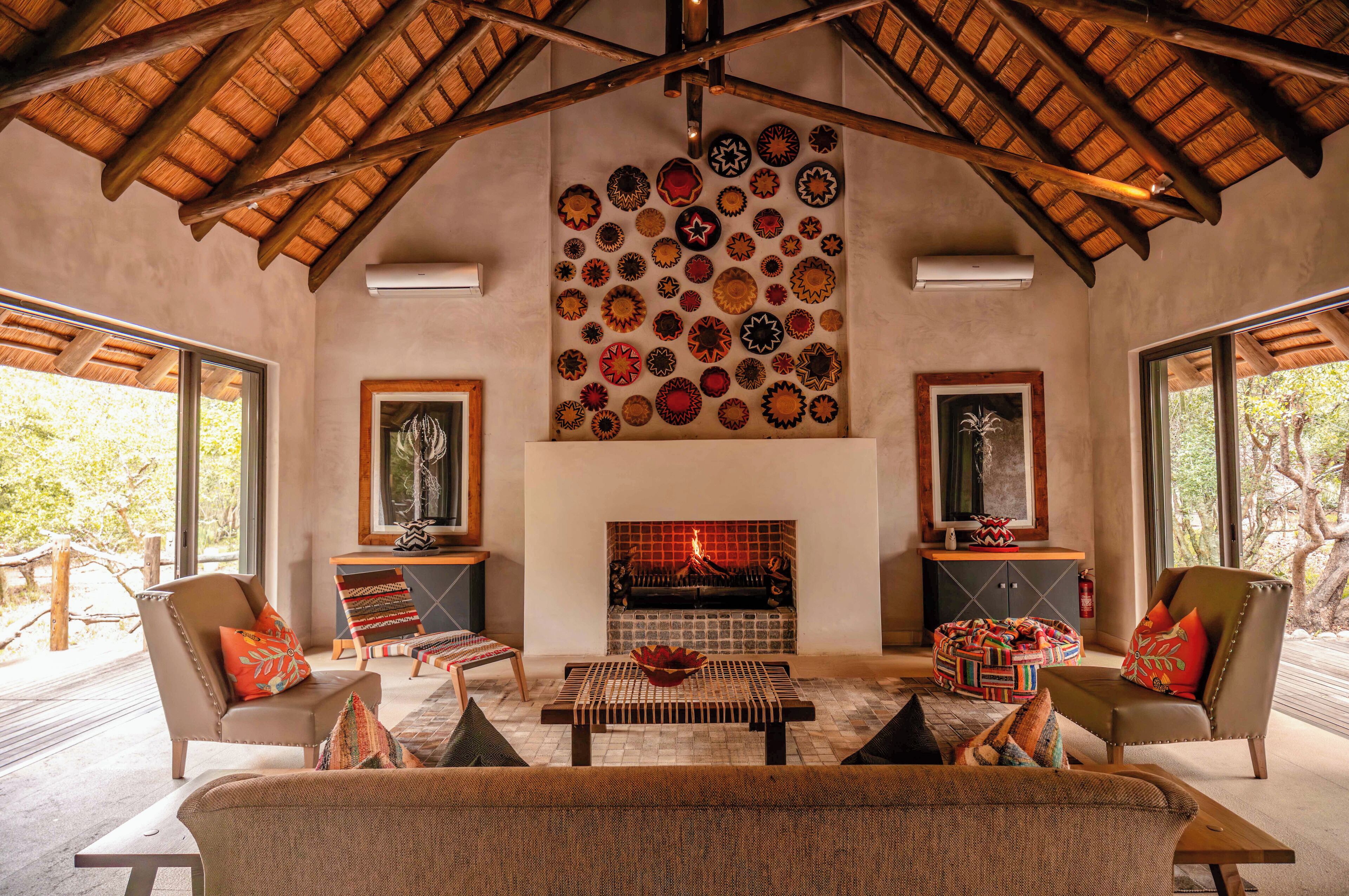 A cozy living room with a fireplace, a wall decorated with circular patterns, and a view of the outdoors.