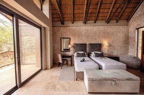 A bedroom with a large sliding glass door, a desk, two beds, and a nightstand with a lamp.