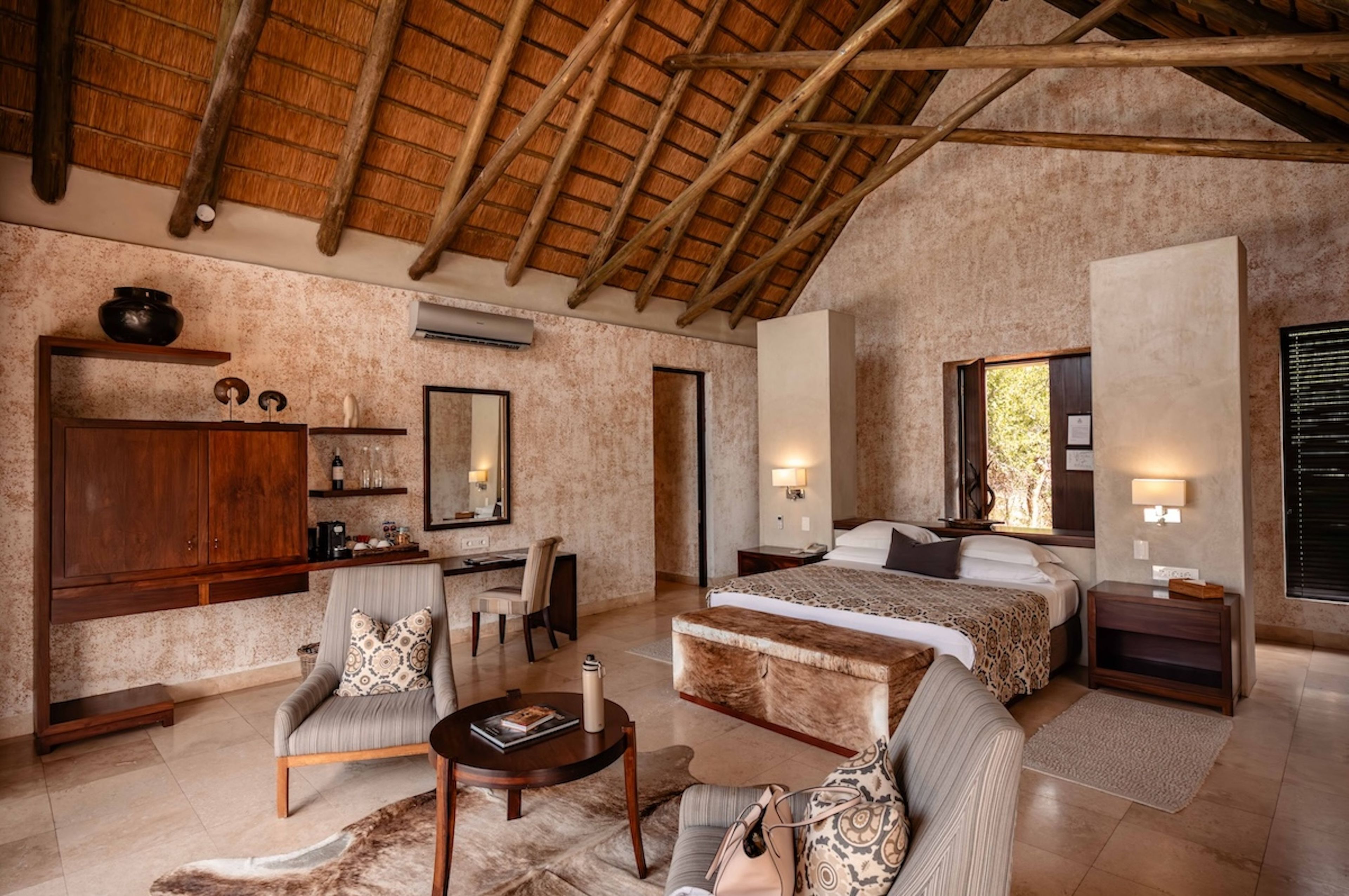 A spacious bedroom with a large bed, a sitting area with a chair and a small table, a wardrobe, and a large mirror.