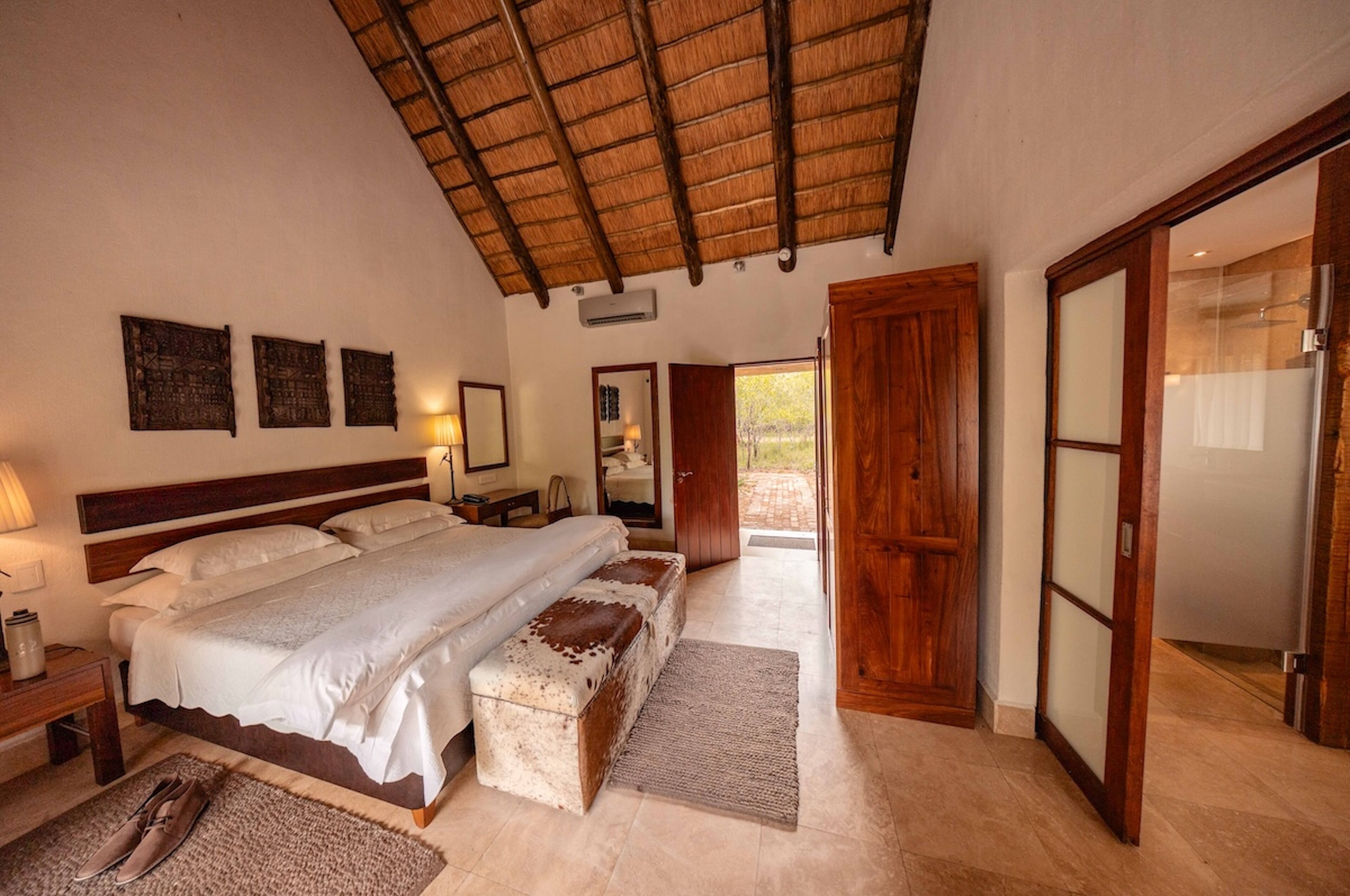 A bedroom with a large bed, wooden headboard, a thatched roof, and a sliding glass door leading to an outdoor area.
