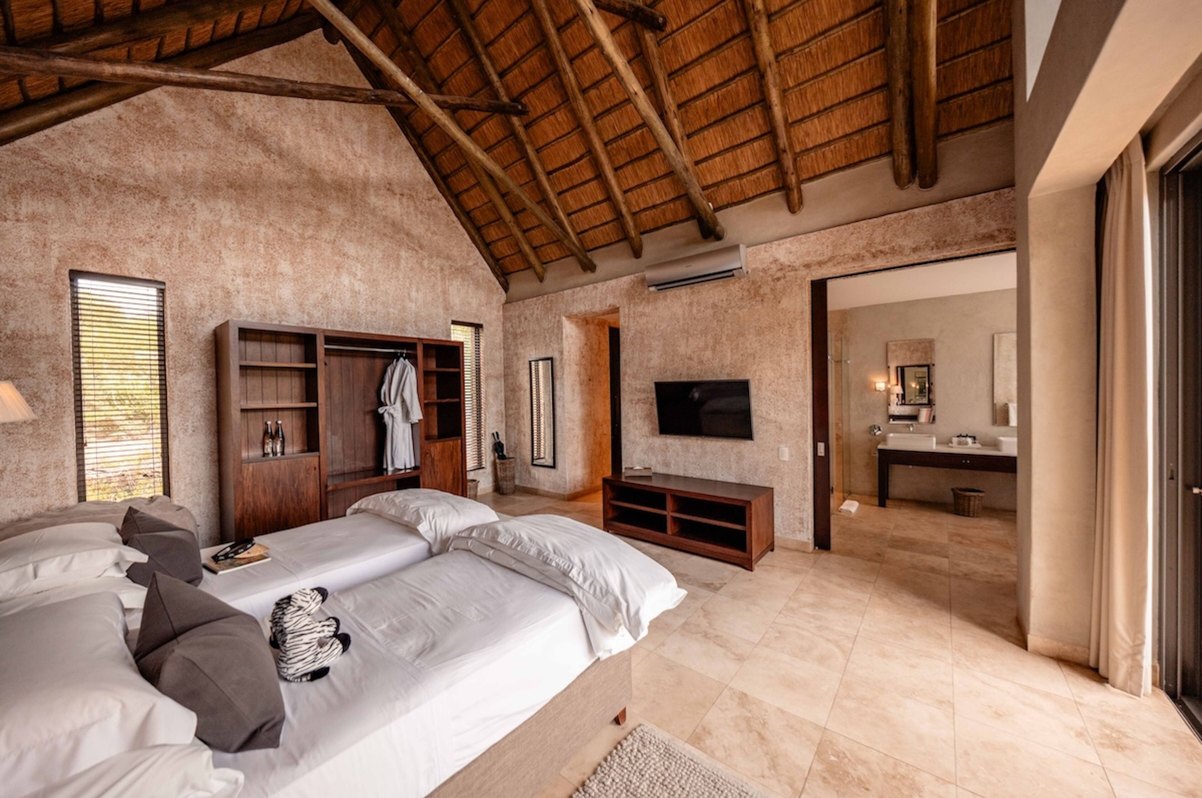 Un'ampia camera da letto con un letto grande, un armadio in legno, una televisione e un bagno visibile tramite una porta aperta.