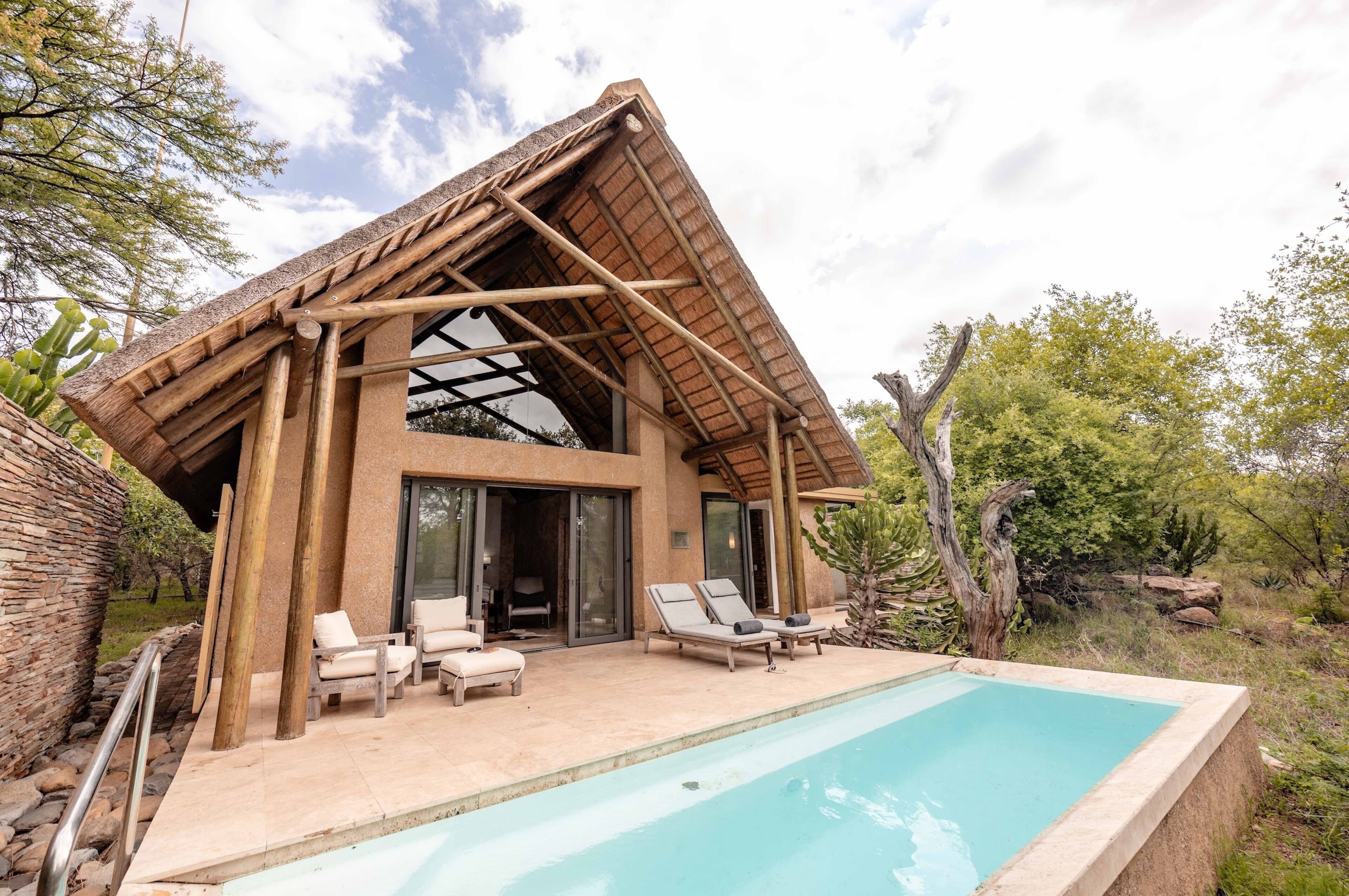 A modern villa with a pool, lounge chairs, and a large glass door entrance.