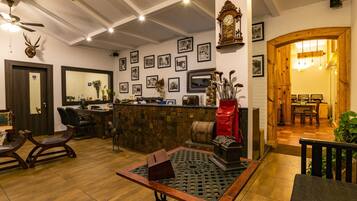 A cozy lobby with a wooden reception desk, framed pictures on the wall, a clock, and a dining area with wooden furniture.