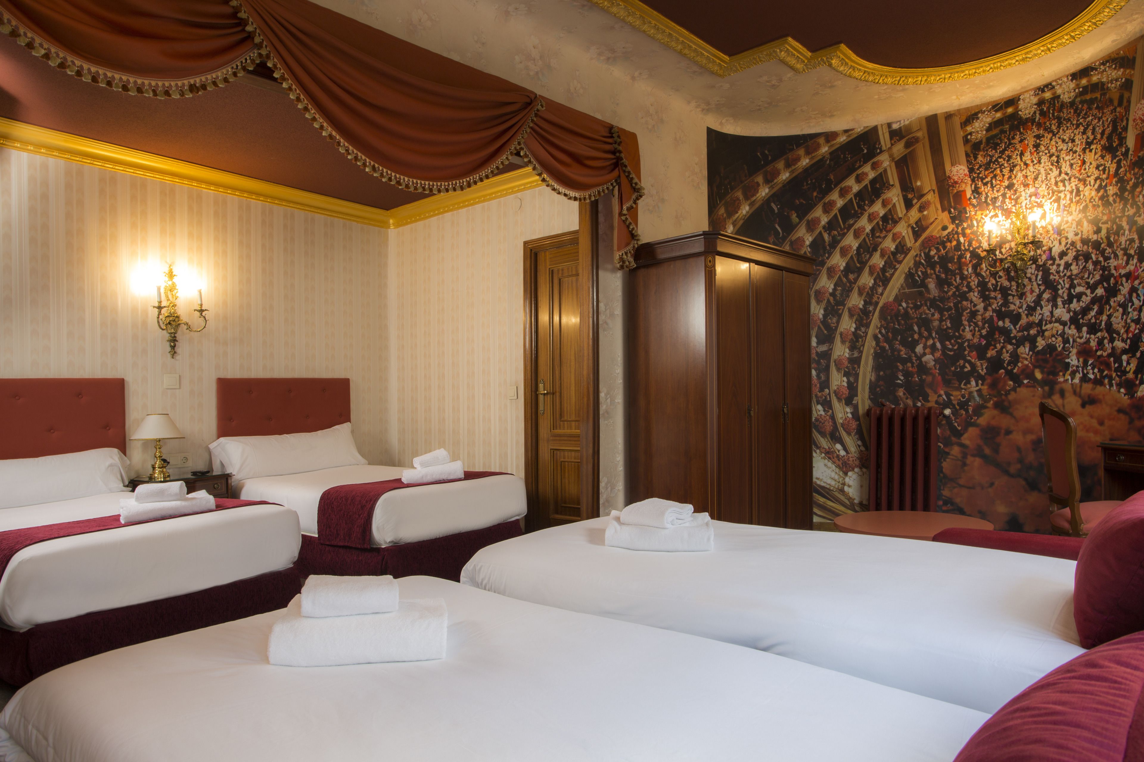 A hotel room with three beds, a chandelier, and a large floral mural on the wall.