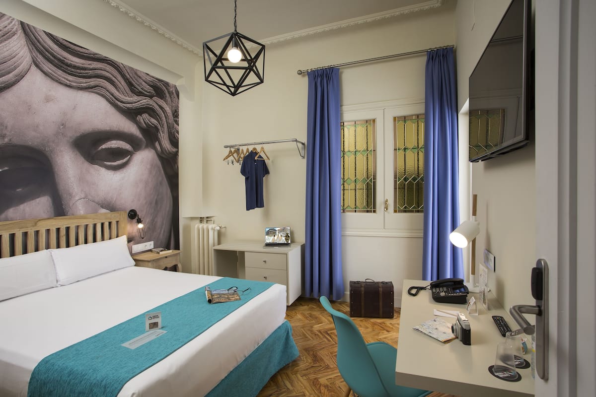 Habitación de hotel con cama, escritorio, silla y un mural grande en la pared.