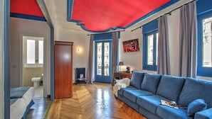 A living room with a blue sofa, wooden flooring, a red ceiling, and a view of the outside. - Casual del Teatro Madrid Hotel by Casual Hoteles (Madrid)