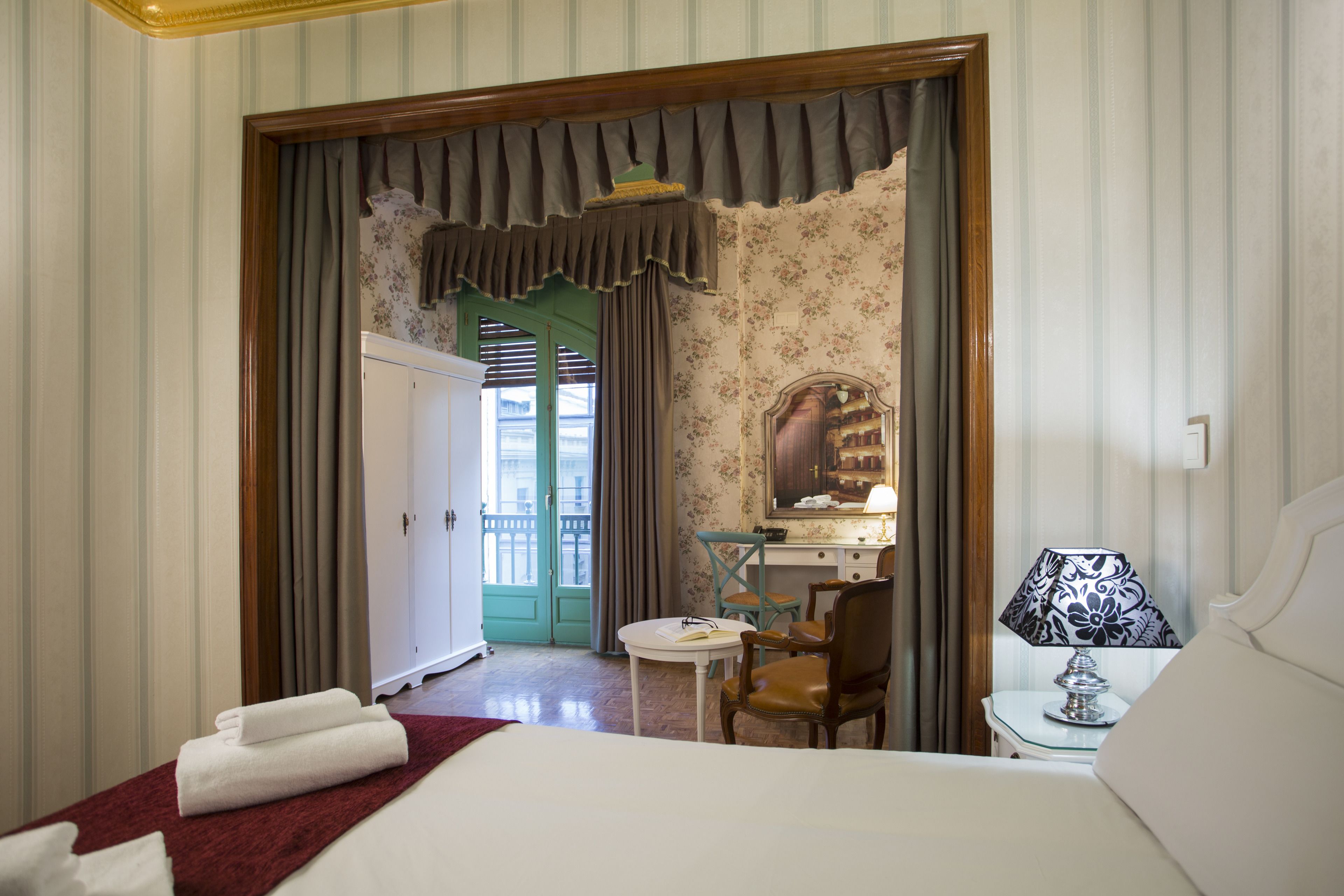 A hotel room with a bed, a desk, a chair, and a table with a lamp.