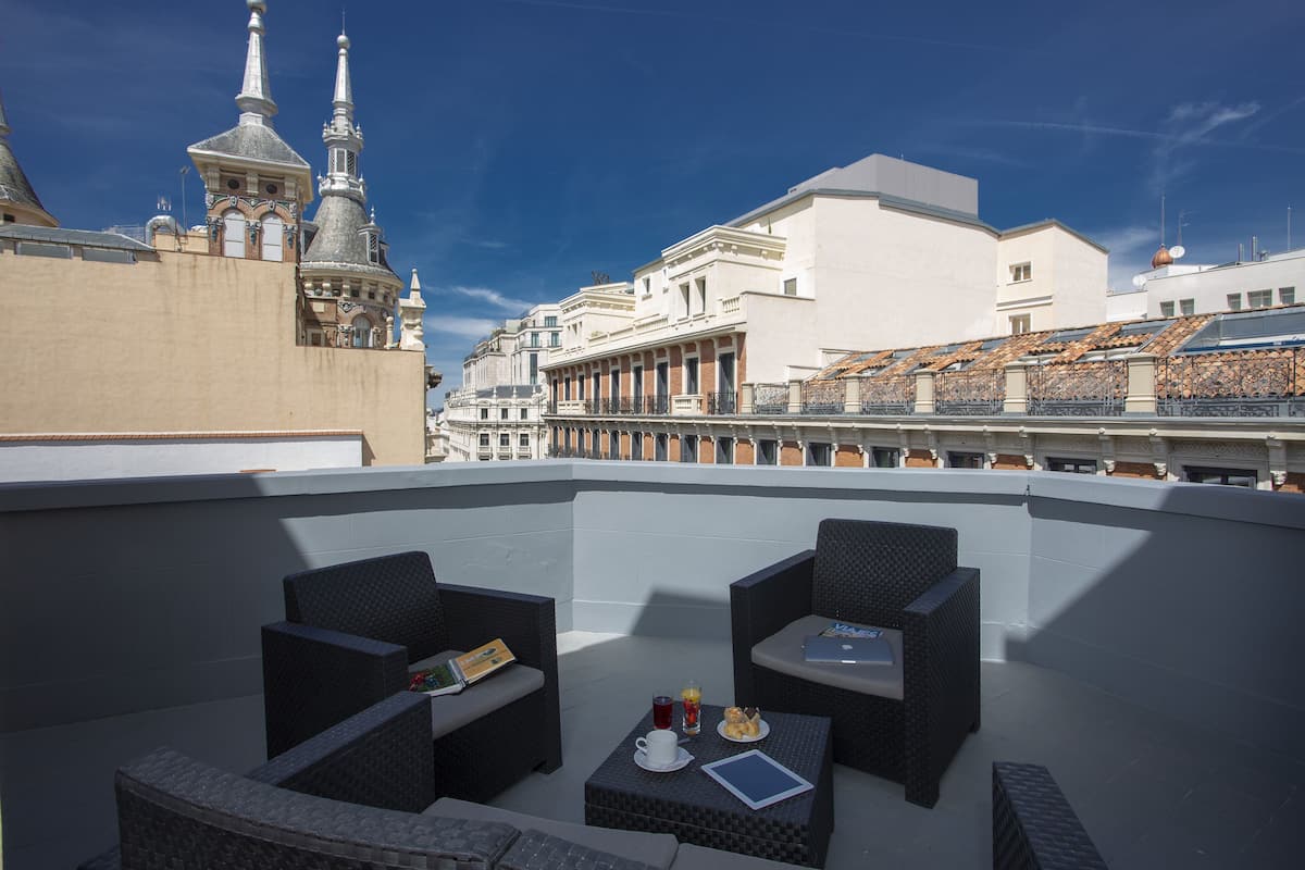 Una terraza en la azotea con mobiliario de mimbre, una mesa con una computadora portátil y una copa de bebida.