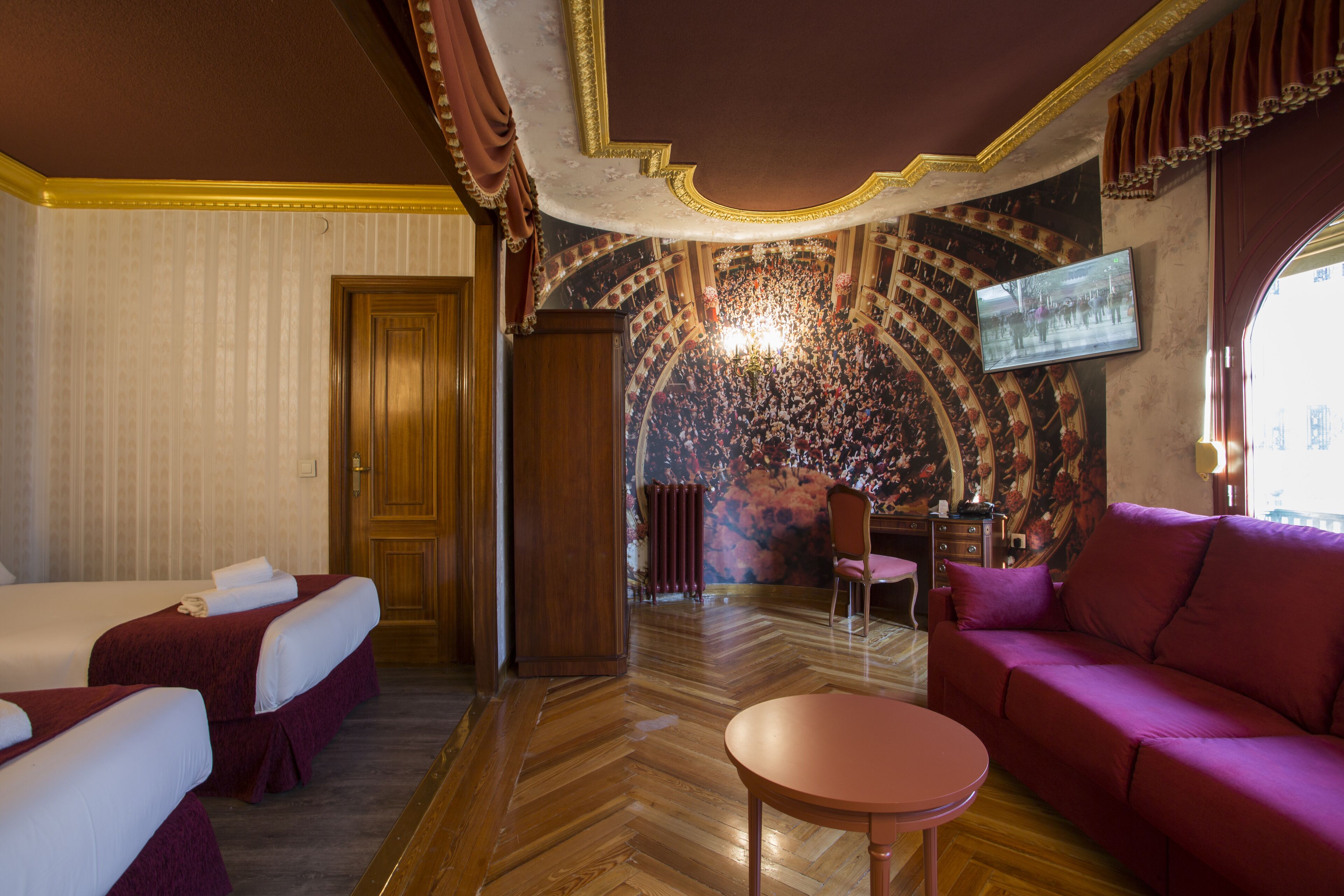 Ein Hotelzimmer mit zwei Betten, einem Sofa, einem Tisch und einem an der Wand befestigten Fernseher.
