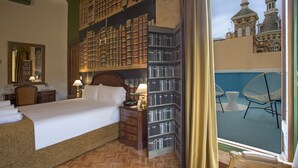 A hotel room with a large bed, a nightstand with a lamp, a bookshelf, and a view of a building with two towers. - Casual del Teatro Madrid Hotel by Casual Hoteles (Madrid)