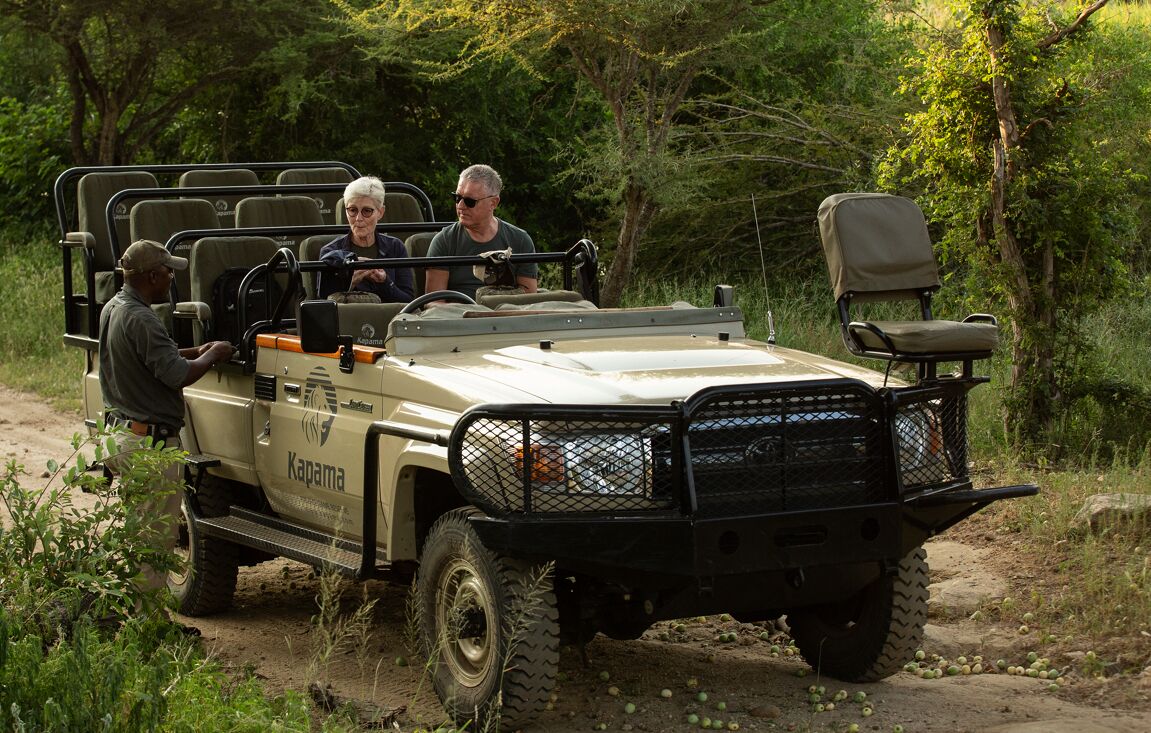 A 4x4 vehicle with passengers, parked on a dirt path surrounded by greenery.