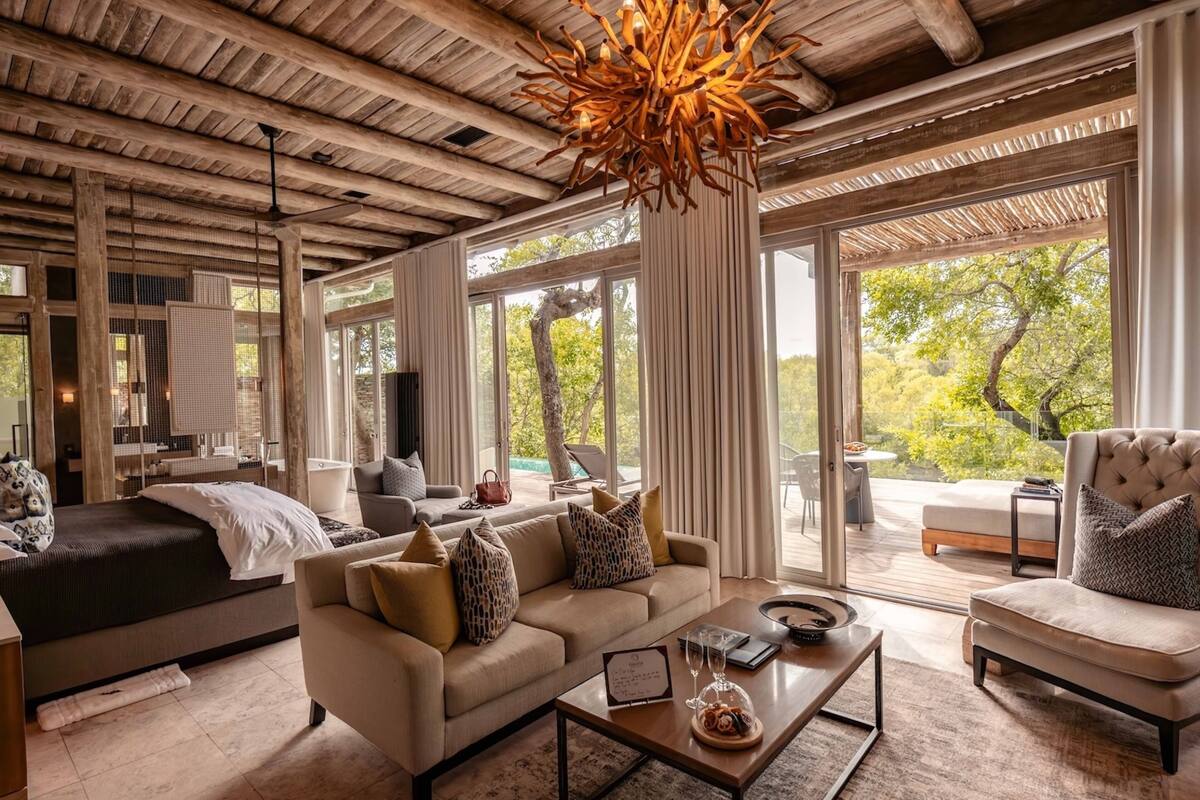 Ein geräumiges Wohnzimmer mit einem großen Sofa, einem Couchtisch und einem Kamin. Große Fenster bieten einen Blick ins Freie.