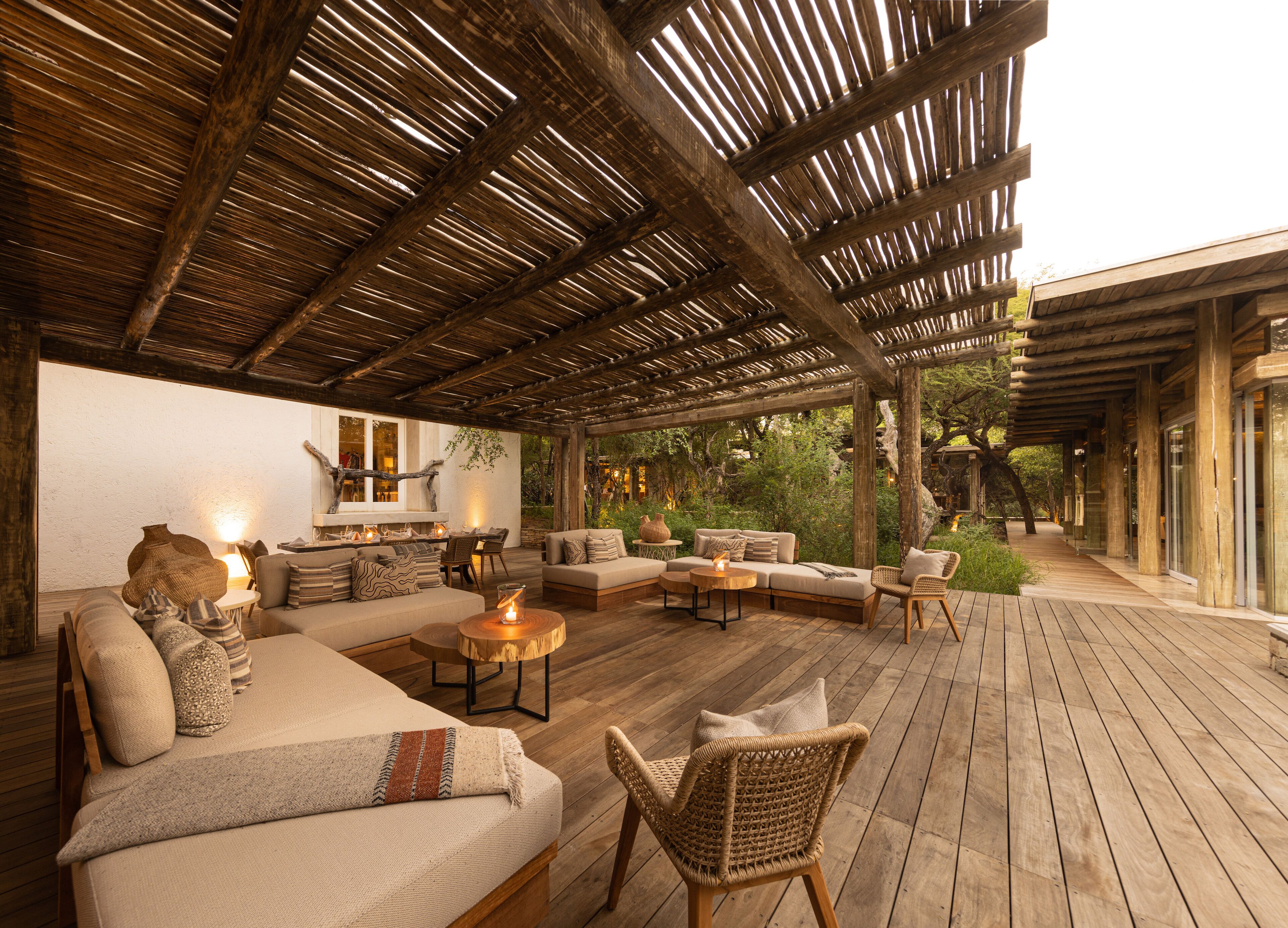 An outdoor covered patio with wooden flooring, a sofa set, a dining table, and a fire pit.