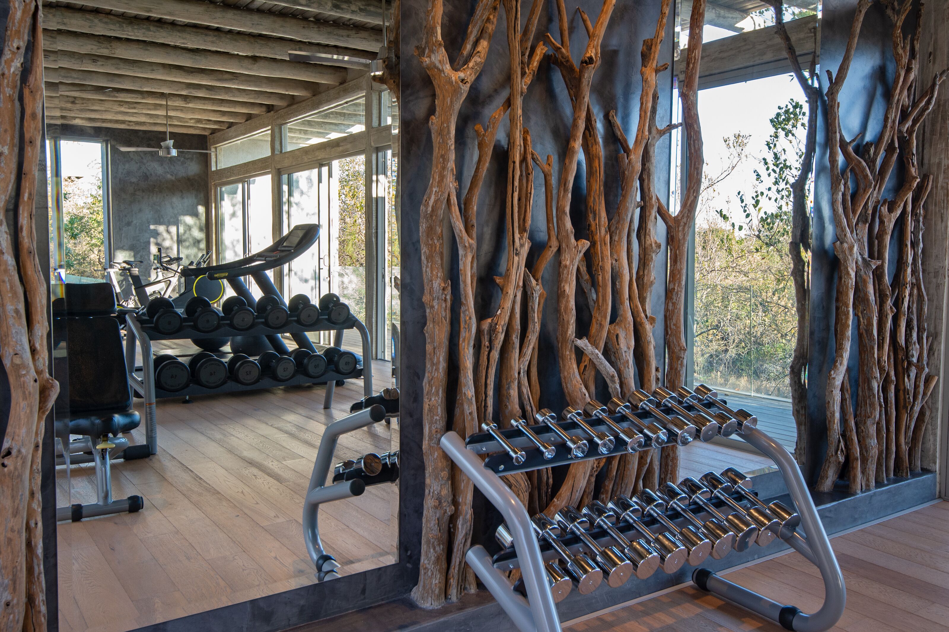 Une salle de sport avec des poutres en bois, un tapis de course, des haltères et un miroir.