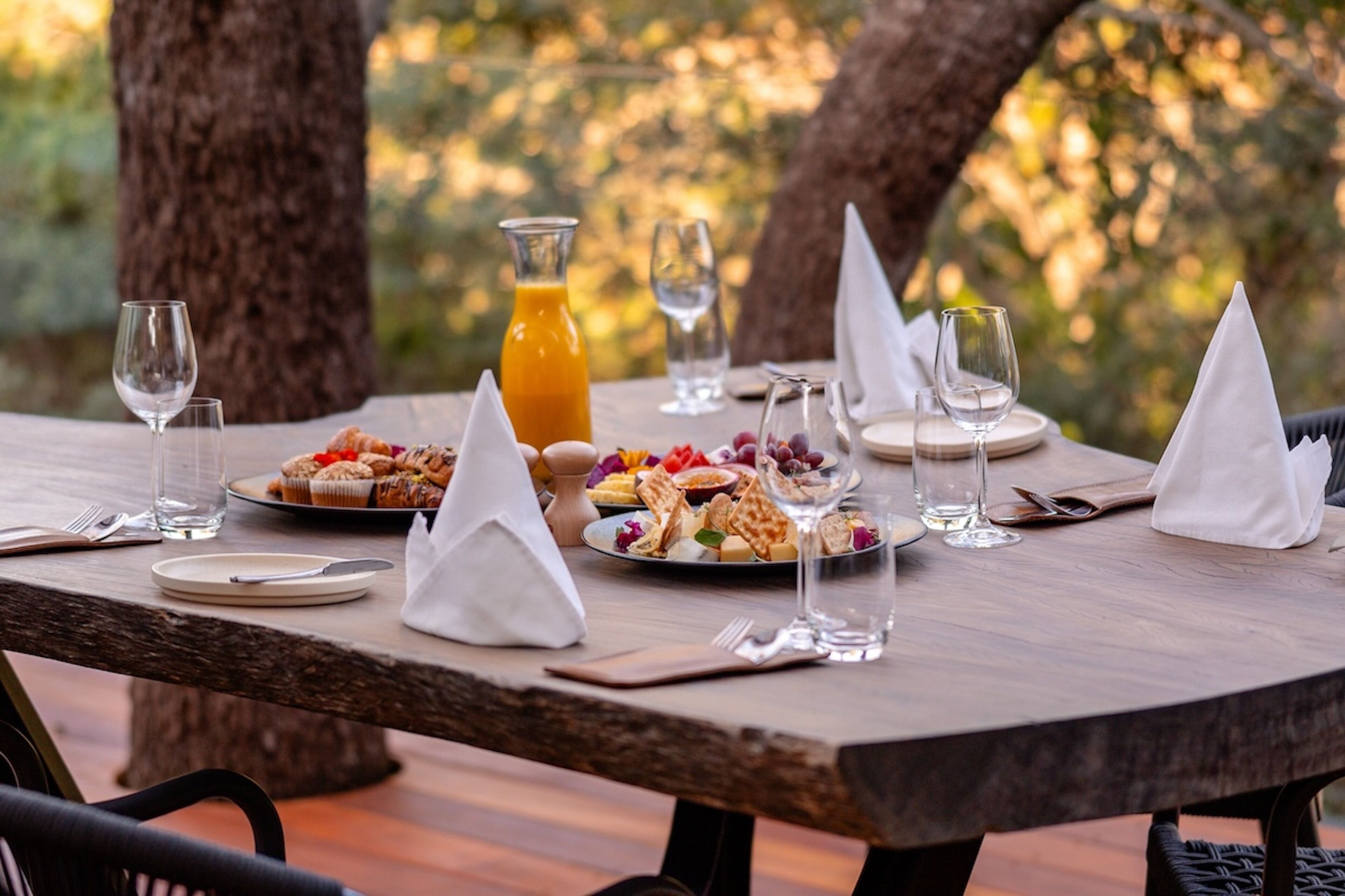 A wooden table set for a meal with plates, glasses, and a pitcher of orange juice.