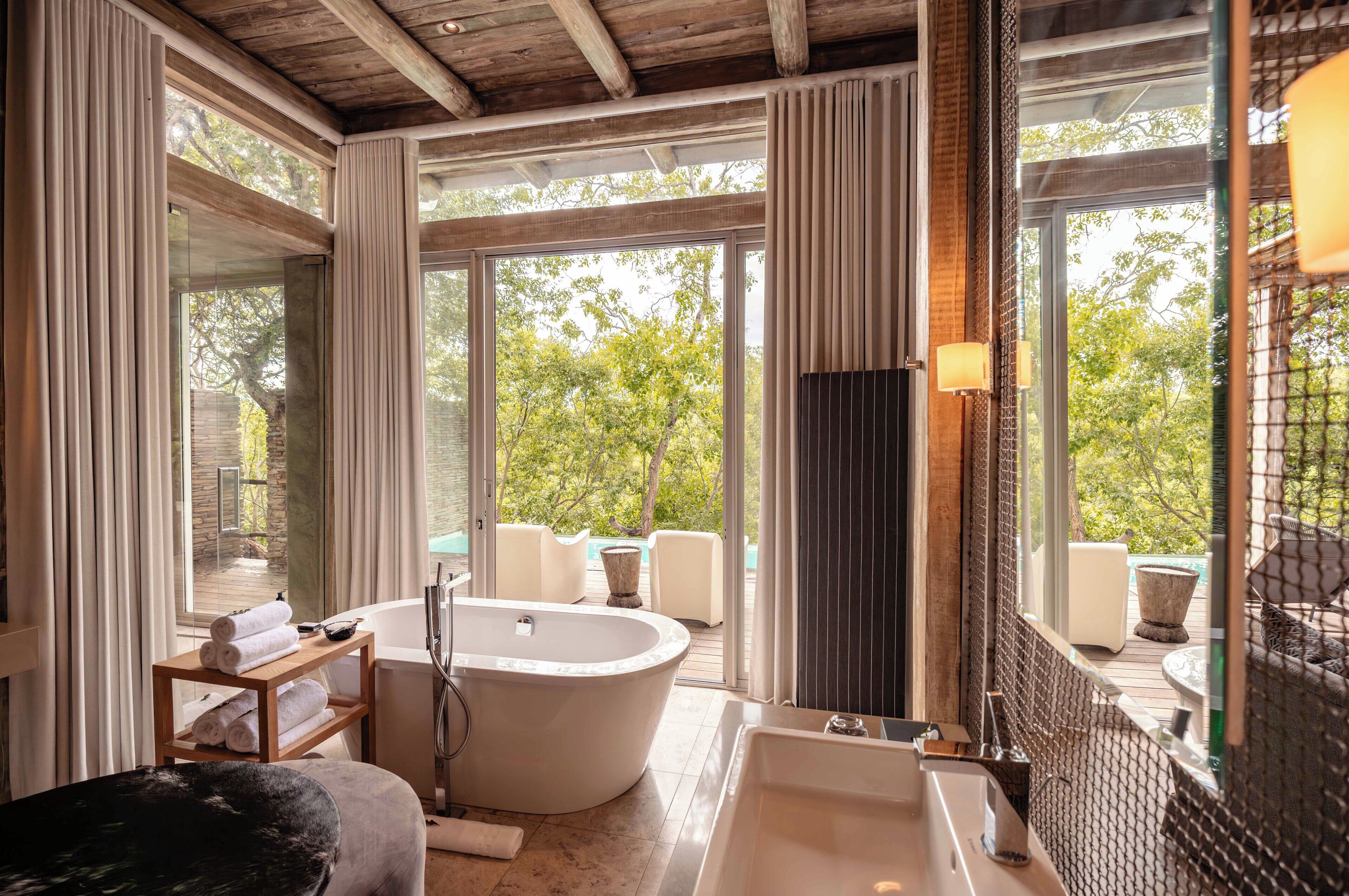 A modern bathroom with a freestanding bathtub, a large window, and a view of the outdoors.
