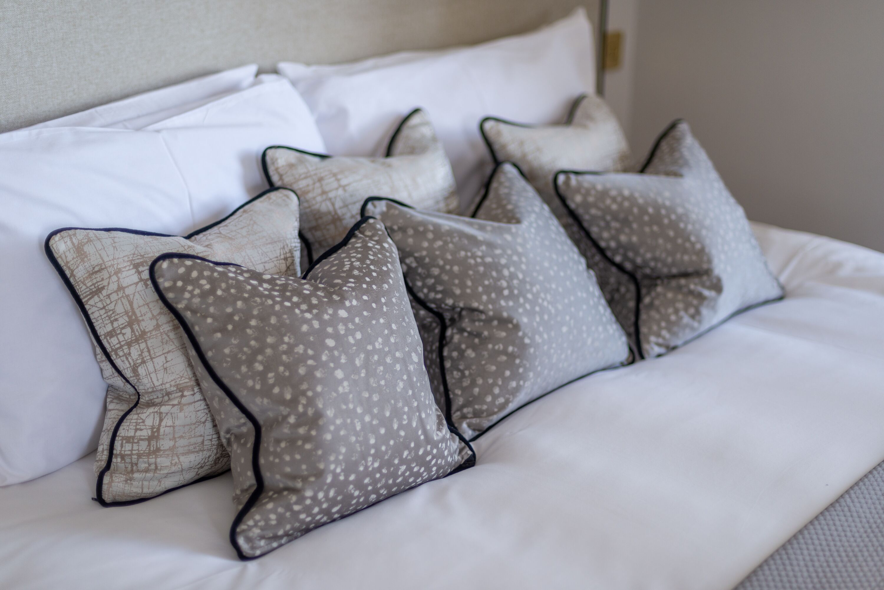 Een net opgemaakt bed met witte beddengoed en meerdere kussens met geometrische patronen.