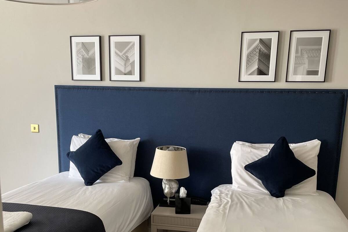A hotel room with two beds, a nightstand with a lamp, and framed pictures on the wall.