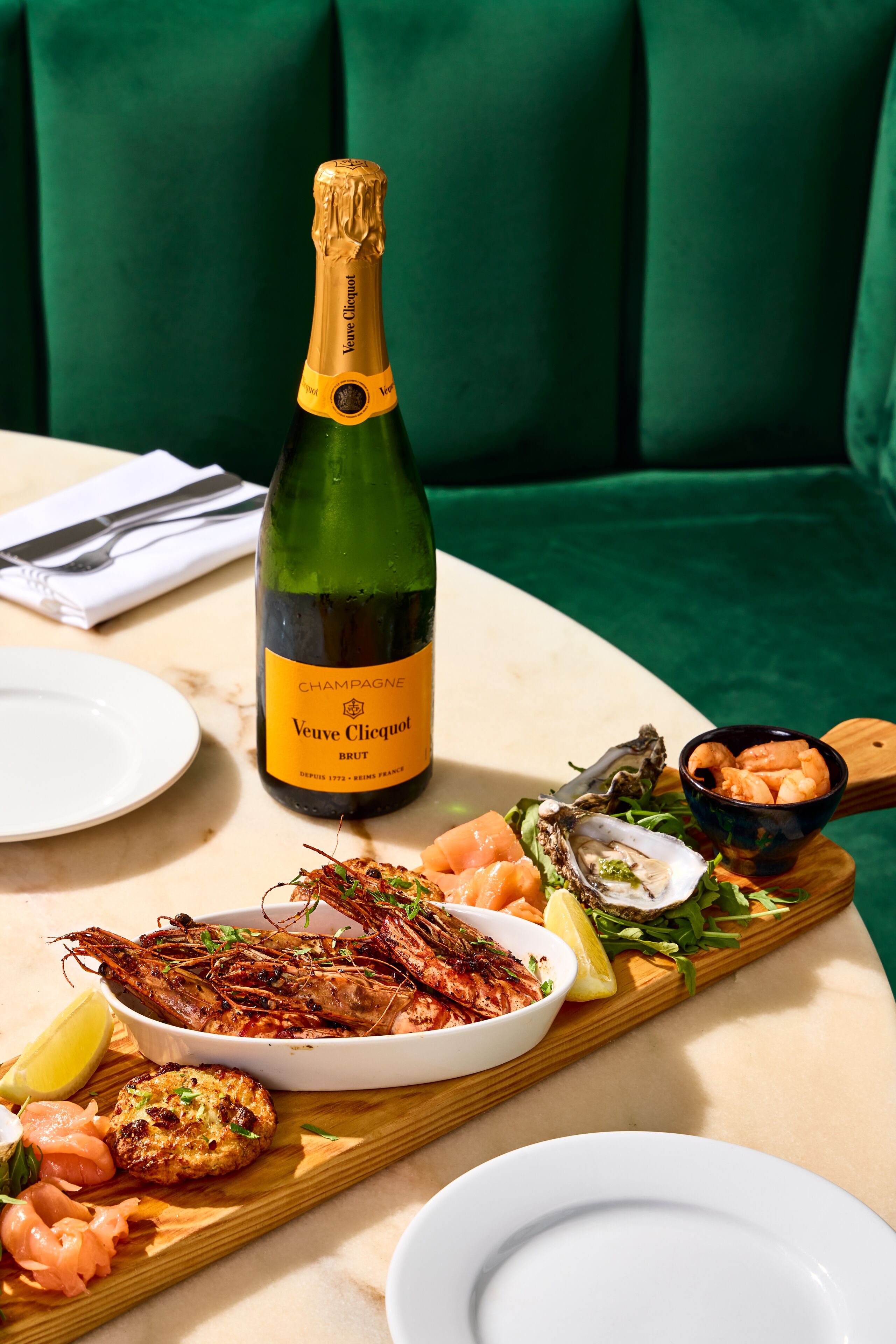 A table with a bottle of Veuve Clicquot Brut champagne, seafood platter, and a bowl of shrimp.